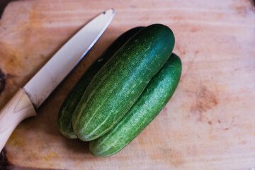 Pile of Fresh cucumbers with kitchen knife on a wooden cutting board, natural presentation, possibly in preparation for slicing or cooking.