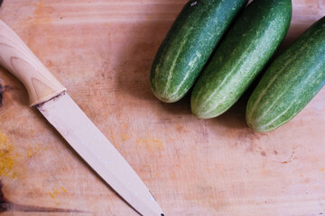 Pile of Fresh cucumbers with kitchen knife on a wooden cutting board, natural presentation, possibly in preparation for slicing or cooking.