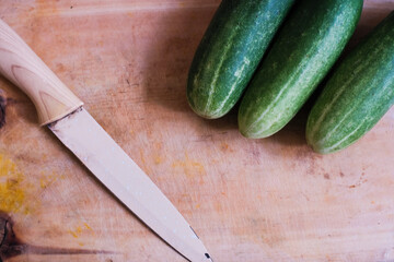 Pile of Fresh cucumbers with kitchen knife on a wooden cutting board, natural presentation, possibly in preparation for slicing or cooking.