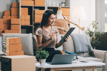 Asian SME business women use laptop computer checking customer order online shipping boxes at home....