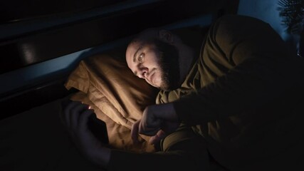 Tired man lying in bed sleepless holding smartphone in hand scrolling social media, suffer sleep disorder in dark bedroom. Man need rest. anxiety, sleeplessness and depression concept - Powered by Adobe