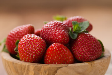Ripe strawberries in wooden bowl on wood background
