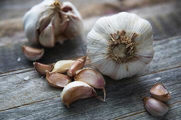 Fresh garlic heads and cloves hover over a wooden table. Fresh peeled garlic and bulbs