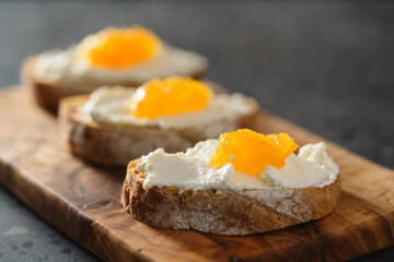 Three ciabatta slices with ricotta and orange marmalade on olive wood board on terrazzo surface