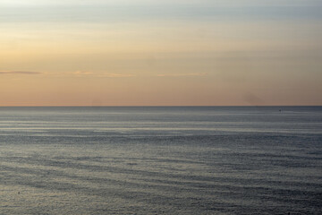 Obraz premium Calm Water extends out to a light blue horizon at early morning sunrise.