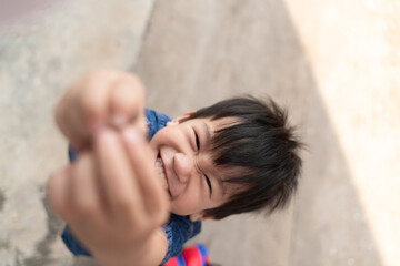 Happy Thai boy smiling and reaching up with his hands, playing outdoors.