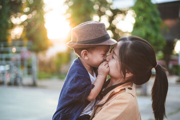 Young boy wearing a hat kissing his mother lovingly on a sunny day.