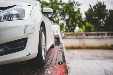 Damaged white car with scratches on a tow truck platform, preparing for transport.