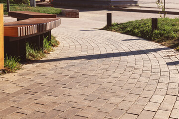 The curved path in the park is paved with gray concrete paving slabs. Selective focus.