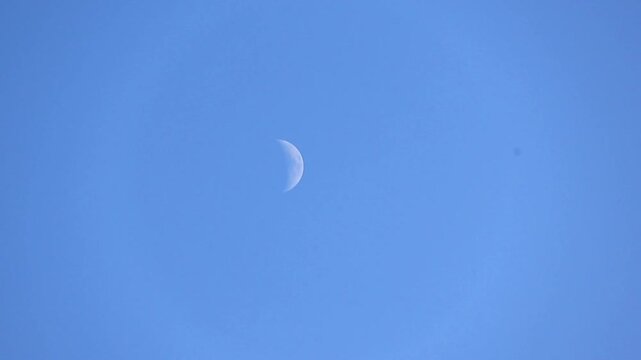 A crescent moon on clear blue sky during daytime.