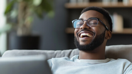 Fototapeta premium A man laughs heartily while enjoying a humorous clip on his laptop in a cozy living room setting during a leisurely afternoon