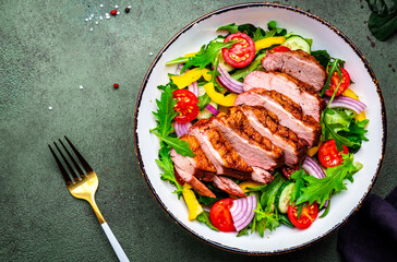 Salad with grilled duck, lettuce and colorful vegetables, green background, top view