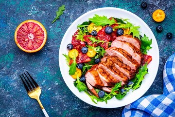 Foodie food salad with grilled duck and citrus, berries and lettuce on blue background, top view