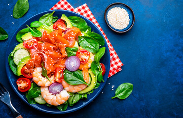 Healthy food salmon salad for keto diet with shrimp, avocado and spinach.  Blue background, top view