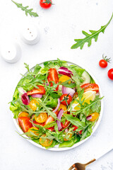 Vegan vegetable salad with tomatoes, cucumber, onion, lettuce and arugula. White background, top view