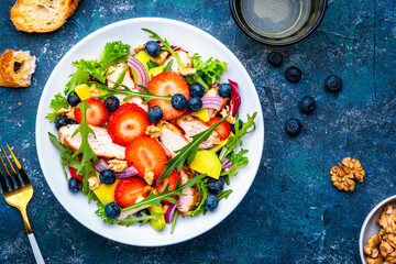 Foodie food salad with strawberry, chicken, arugula, blueberries, avocado and walnuts, blue table., top view