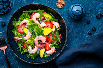 Foodie food shrimp salad with strawberry, arugula, lettuce, avocado and red onion, blue background