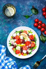 Greek salad with feta cheese, olives, tomatoes, lettuce, paprika, cucumber and onion. Blue background, top view