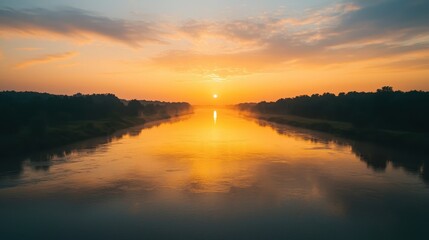 Obraz premium A serene sunset over a calm river, reflecting vibrant orange and yellow hues, bordered by lush greenery.
