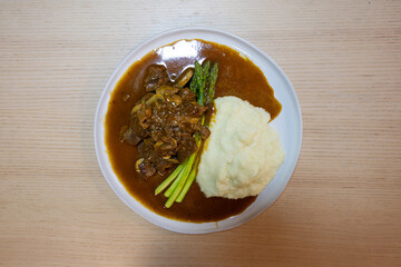 A plate of beef stew, asparagus, and mash potato.