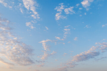 A clear blue sky with light, scattered small clouds at dawn stretching across the horizon. The sky...