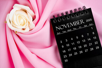 November 2025 desk calendar black color and rose on textile background.