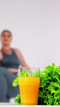 Vertical video. A fit, radiant woman enjoys a refreshing juice after her workout against a clean, light backdrop. Perfect for showcasing a healthy lifestyle and the synergy of fitness and nutrition. 