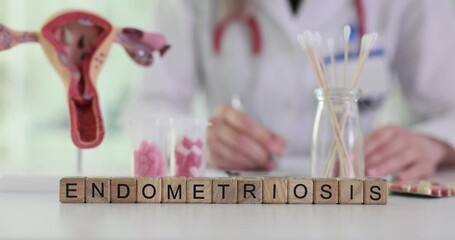 Word Endometriosis on letter blocks and blurry view of doctor writing at table. Anatomical model of female reproductive system and disease name