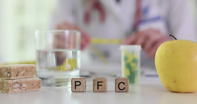 Inscription PFC for proteins fats carbohydrates on nutritionist workplace. Woman doctor holds measuring tape over table with food supplements