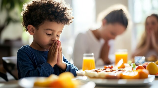 Young child praying at breakfast table with family in bright morning light - Powered by Adobe