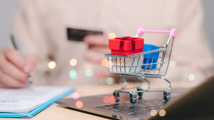 Miniature shopping cart filled with colorful gifts sits on laptop keyboard, signifying joy of...