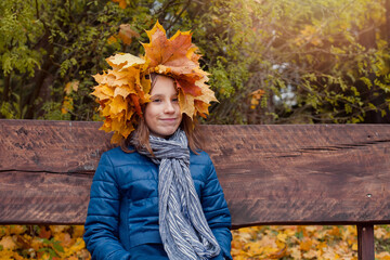 Happy smiling young child girl in autumn leaves wreath, fall season