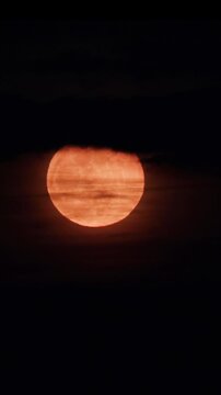 Full moon rising in the night sky and hiding behind dark clouds. Gloomy night skyscape in moonlight. Halloween evening, real video footage Supermoon