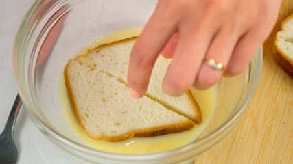 Woman soaking bread in whisked egg in glass bowl to fry toasts cooking on kitchen at home, hands close-up. Preparing snack fast food. Ingredients recipe cuisine culinary. Domestic homemade meal.