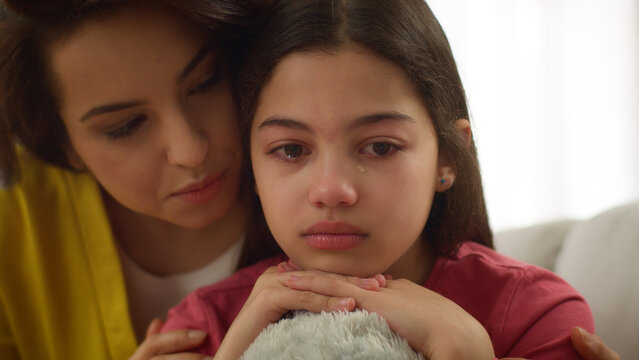Close up Caucasian crying sad anxious depressed little girl child kid daughter cry upset by school problems abuse bullying while caring loving mother sister woman female comforting stroke hair indoors