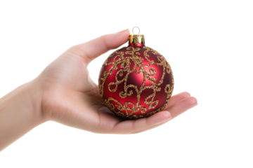 Hand holding a red and gold christmas ornament with intricate designs on a transparent background