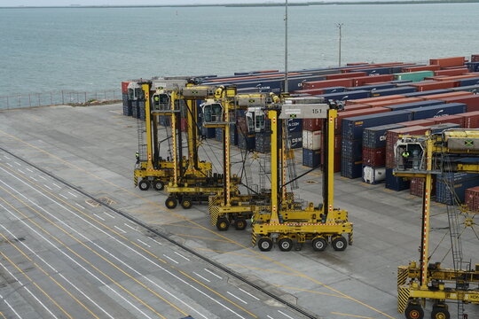 Kingston, Jamaica - 05 29 2024: Yellow straddle carriers are lined up at the Kingston Freeport container terminal, poised beneath gantry crane. Surrounding them are containers from various shippers.