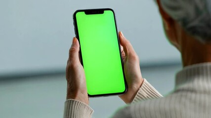 Elderly gray-haired woman making video call at smartphone camera green screen. Senior lady talking and listening during video chat with friends or colleagues. Over shoulder mobile phone screen view.  - Powered by Adobe