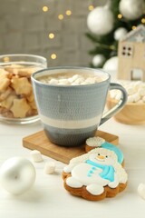 Delicious cookie in shape of snowman, cup with cocoa and Christmas decor on white wooden table