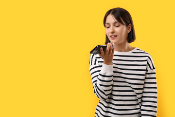 Beautiful woman recording voice message via smartphone on yellow background, space for text