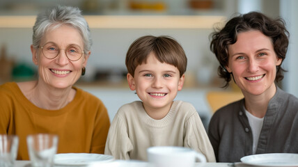 Happy family portrait featuring three generations. Elderly woman, young boy, and adult woman smiling indoors at home.