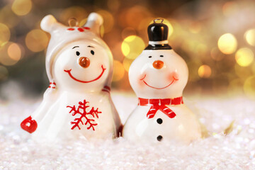 Cute snowman figures against blurred Christmas lights, closeup. Bokeh effect