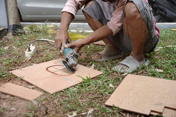 Construction worker cutting floor tiles with angle grinder at construction site with dirty hands. Cutting large ceramic tiles with special tools.  Hard worker concept. Sstkindustry