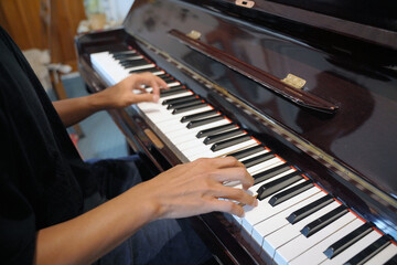Obraz premium Close-up of a young Asian man touching the piano keys with his fingers, playing a musical composition while playing a grand piano in a cafe.