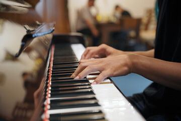 Close-up of a young Asian man touching the piano keys with his fingers, playing a musical composition while playing a grand piano in a cafe. © Daniel Pawer