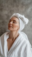 Obraz premium Serene mature woman in a white robe and towel, eyes closed, experiencing peaceful spa and self-care moment.