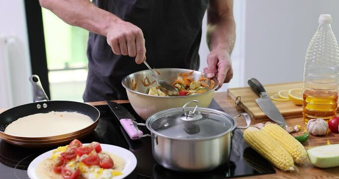 Culinarian mixes salad dressed with olive oil in iron bowl using tablespoon. Home cooking in surrounding of contemporary kitchen slow motion