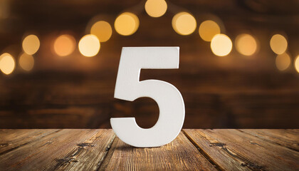 White number 5 five on wooden background, bokeh with golden lights. Holiday and celebration