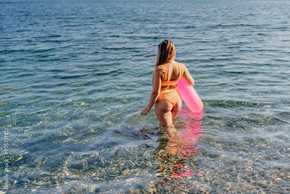 Canvas Prints A woman in a bikini is walking in the ocean with a pink inflatable tube