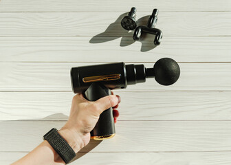 Close-up of woman's hand demonstrating portable massage gun on a white background.
